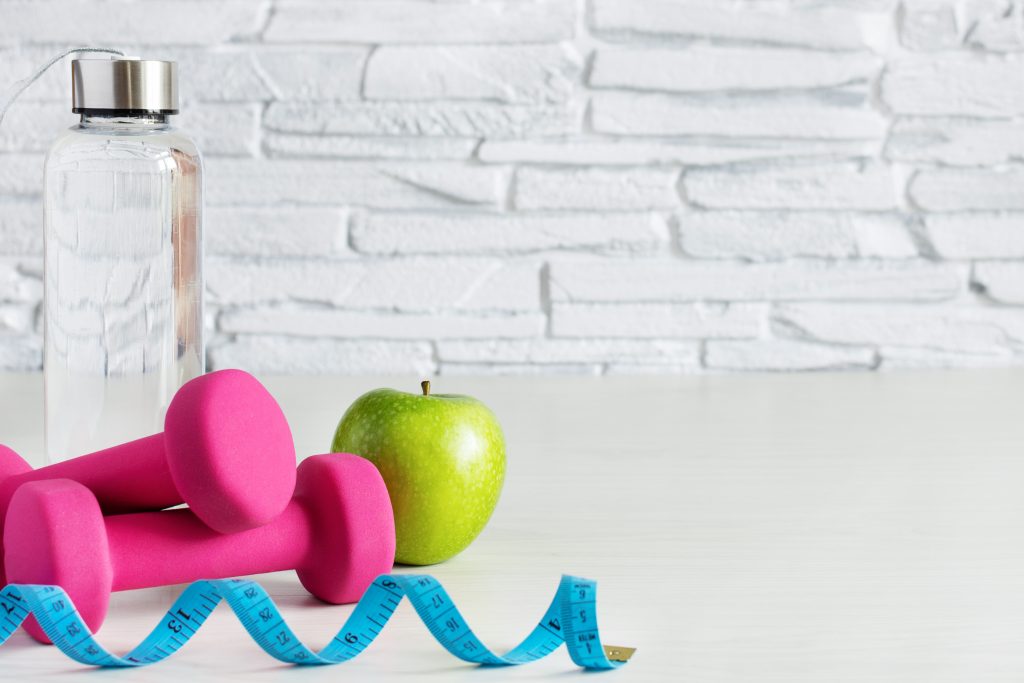 healthy lifestyle with weights, water, tape measure, and green apple