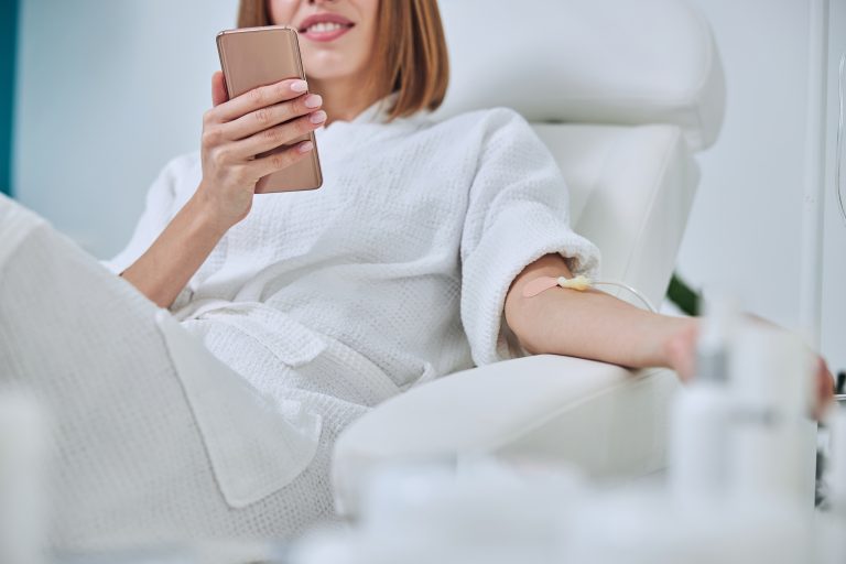 woman receiving iv therapy while she is on her phone