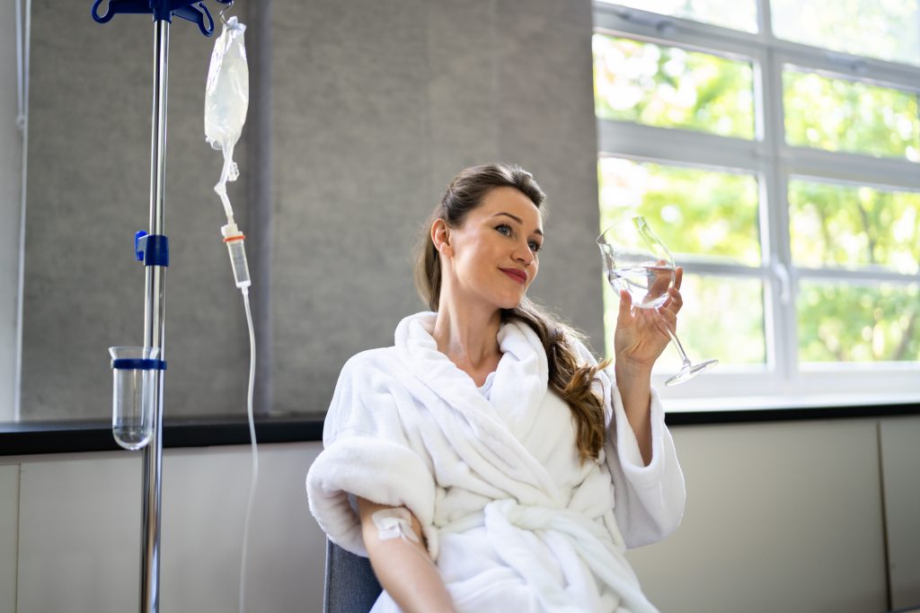 woman receiving iv therapy while holding a glass of water