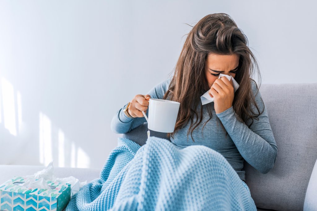 woman sick on couch with blanket, mug, and tissues